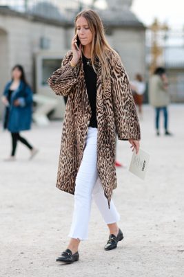 A guest pairs a leopard coat with cropped denim jeans and Gucci loafers outside the Jacquemus show.