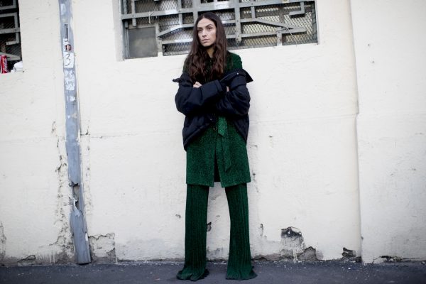 A black puffer jacket worn off the shoulder provides a visual break from head-to-toe metallic green lurex.