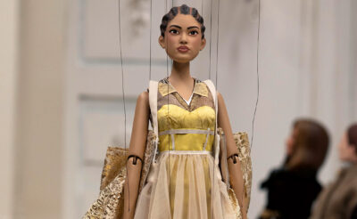 A doll walks the Moschino runway in place of models, wearing a gold dress