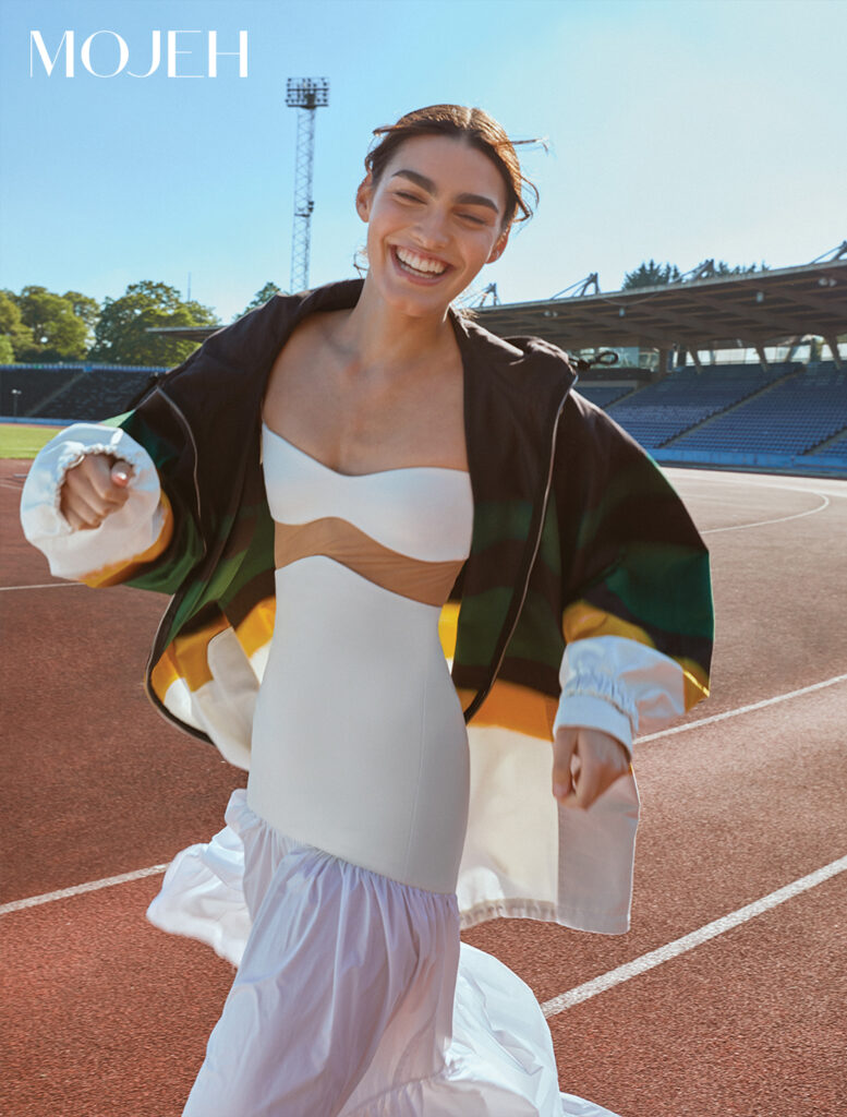 The Shoot: Athleisure, But Not As You Know It; Model wears David Koma and Dries Van Noten, smiling and standing on a running track