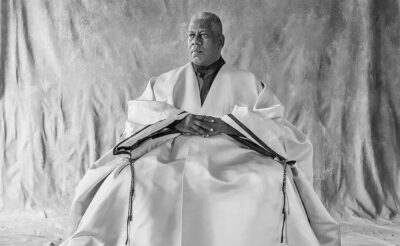 Black and white photograph of André Leon Talley sitting in a studio wearing a robe