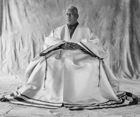 Black and white photograph of André Leon Talley sitting in a studio wearing a robe
